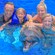 A young family of 4 smiles while posing in the water with a dolphin